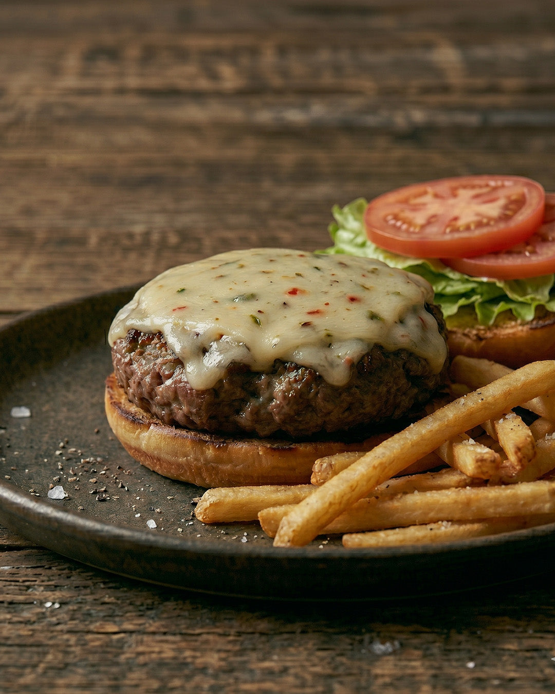 Hamburger with cheese and tomato on a bun, served with fries on a wooden table