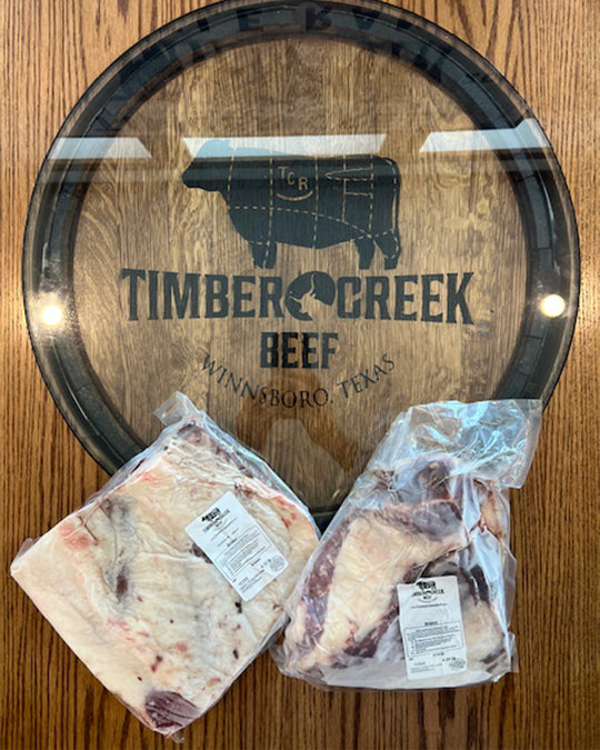 Two packages of raw meat on a wooden surface with a 'Timber Creek Beef' branded cutting board.