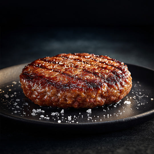 Grilled hamburger patty on a black plate with salt crystals