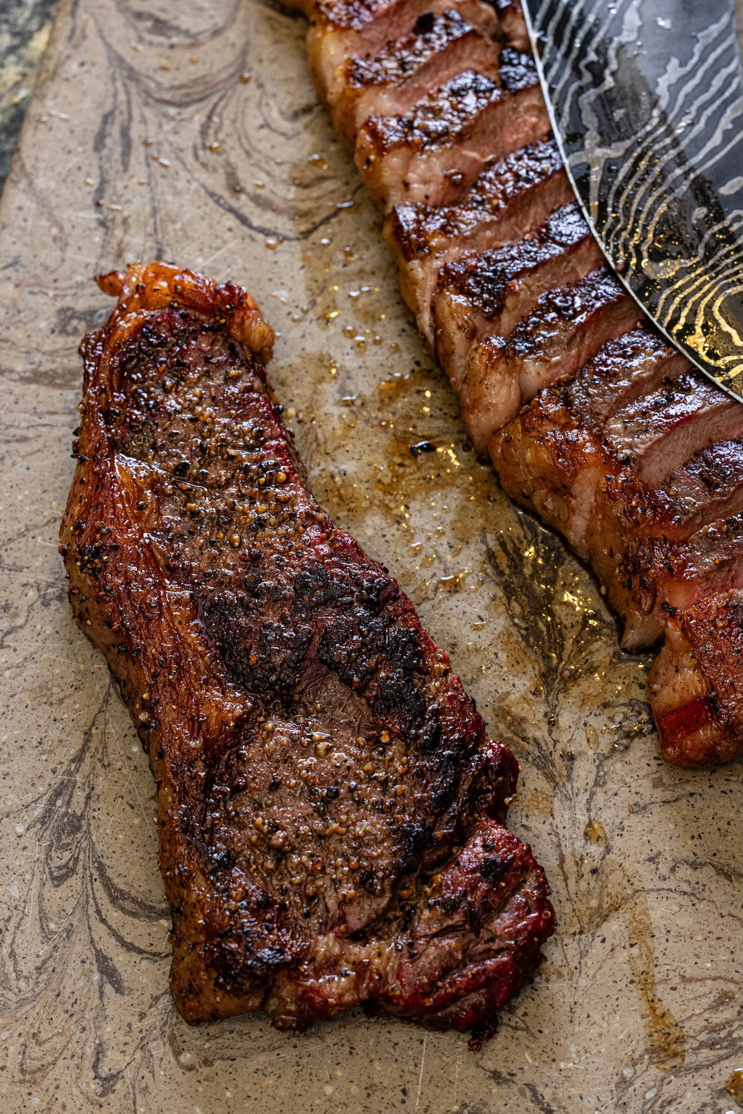 Two grilled steaks on a textured surface with a decorative knife.