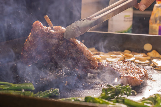 Person grilling meat with tongs over a smoky grill
