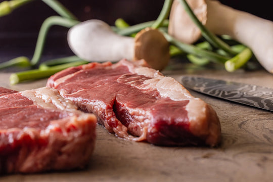 Raw beef steaks on a wooden surface with green onions and garlic.
