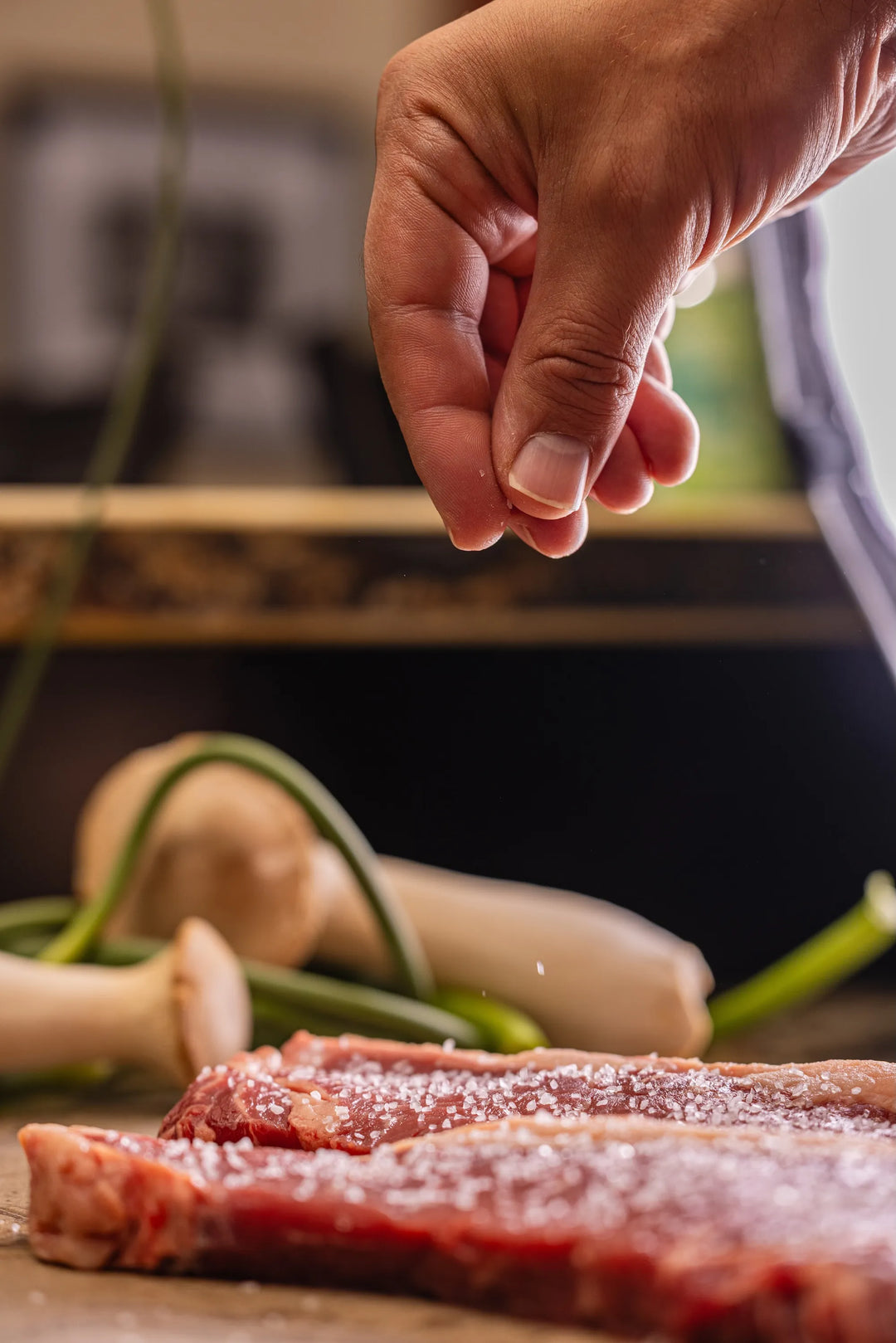 Hand seasoning raw meat with salt on a wooden cutting board.
